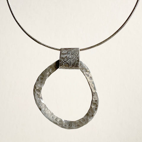 Closed shape hammered silver pendant with floral detailed bail.