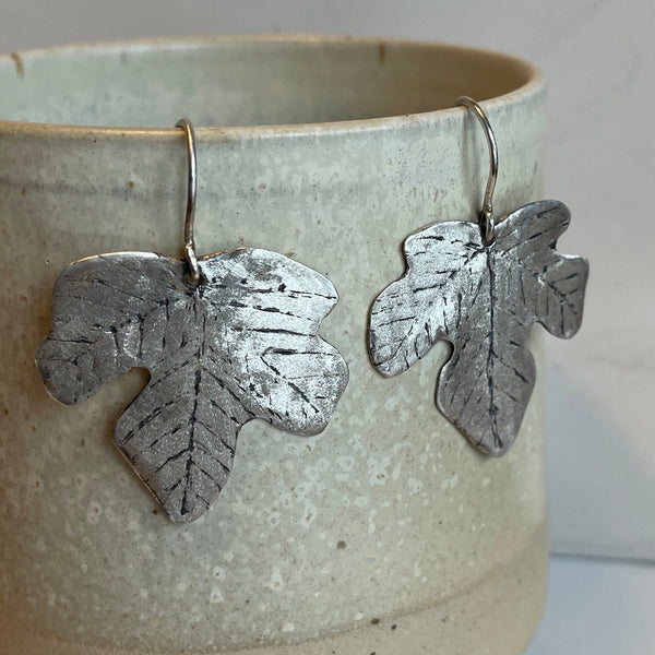 Silver leaf-shaped earrings hanging from a ceramic mug.