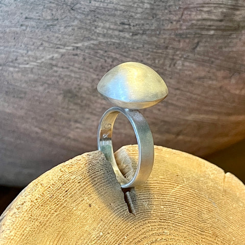 Silver ring with a  dome shaped top on a wooden surface