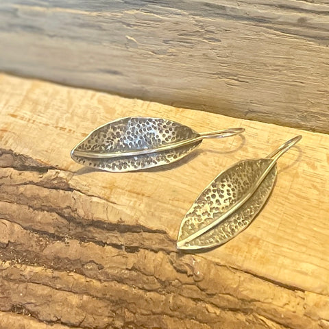 Hammered sage leaf-shaped earrings on a wooden surface