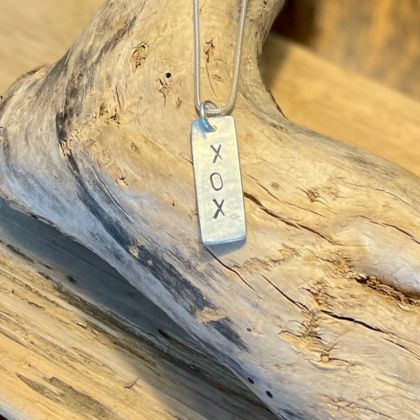 Silver necklace with a tag featuring 'XOX' on a piece of driftwood.