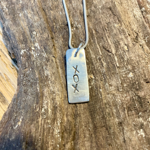 Silver pendant with 'XOX' on a wooden surface