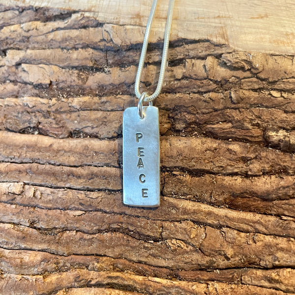 Silver pendant with 'PEACE' engraved on a wooden surface
