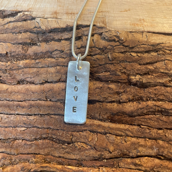 Silver 'LOVE' pendant necklace on a wooden surface