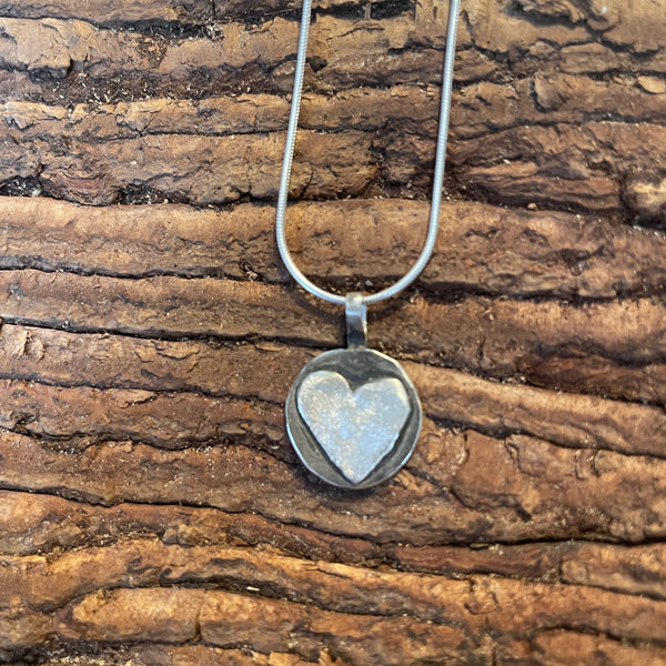 Heart-shaped silver pendant on a chain against a wooden background