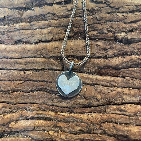 Silver necklace with a heart-shaped pendant on a wooden surface