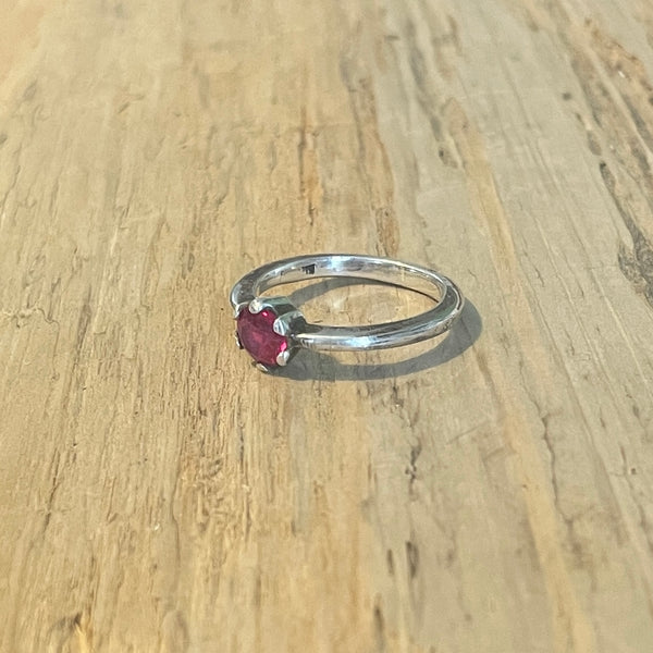 Silver ring with a red  ruby gemstone on a wooden surface