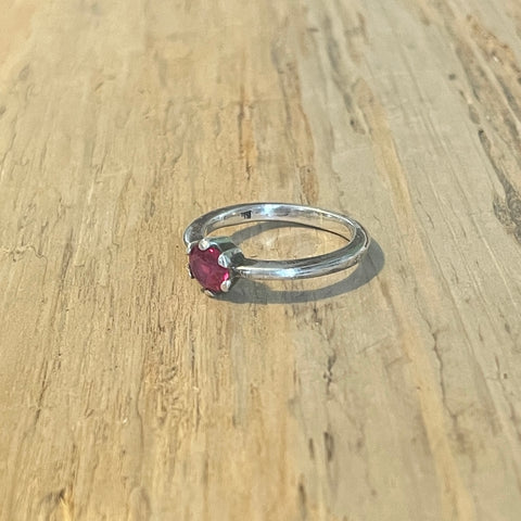 Silver ring with a red  ruby gemstone on a wooden surface